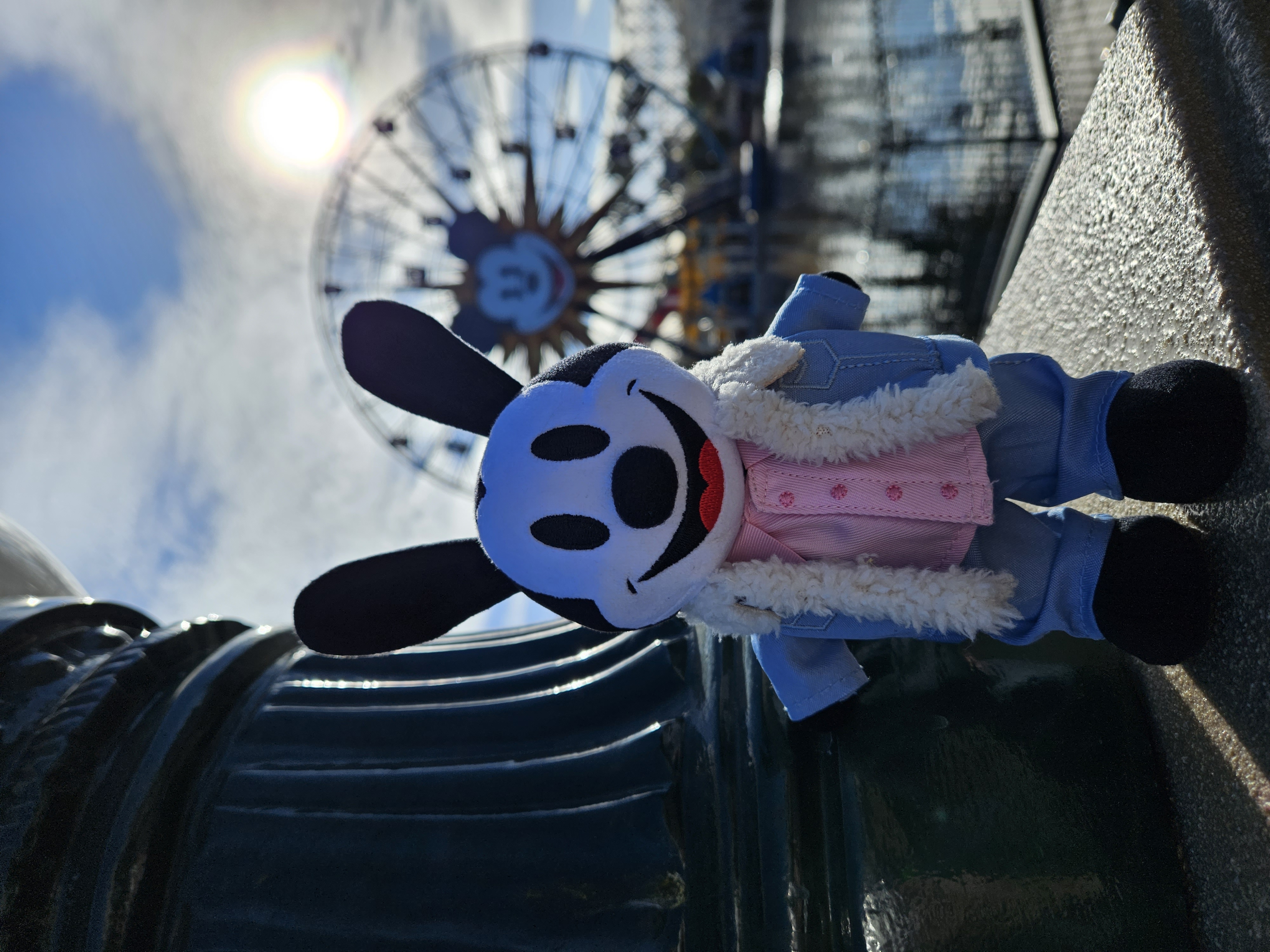 An Oswald the Lucky Rabbit nuiMOs doll dressed up in a Valentine's outfit posing next to the Pixar Pal-A-Round in the distance a